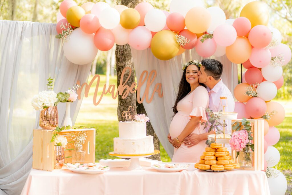couple fêtant sa babyshower avec un fond de ballons colorés et le gâteau